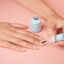 A person applying Gel Break to their nails with a bottle in the background on a pink surface.
