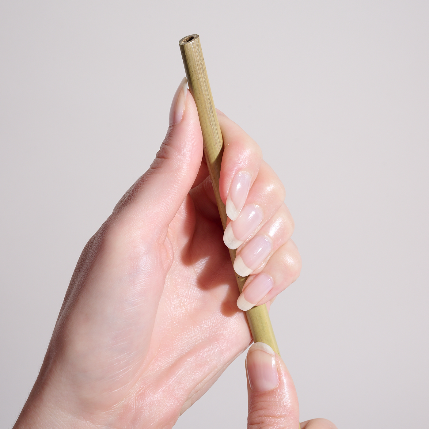 Hand holding a bamboo straw against a plain background