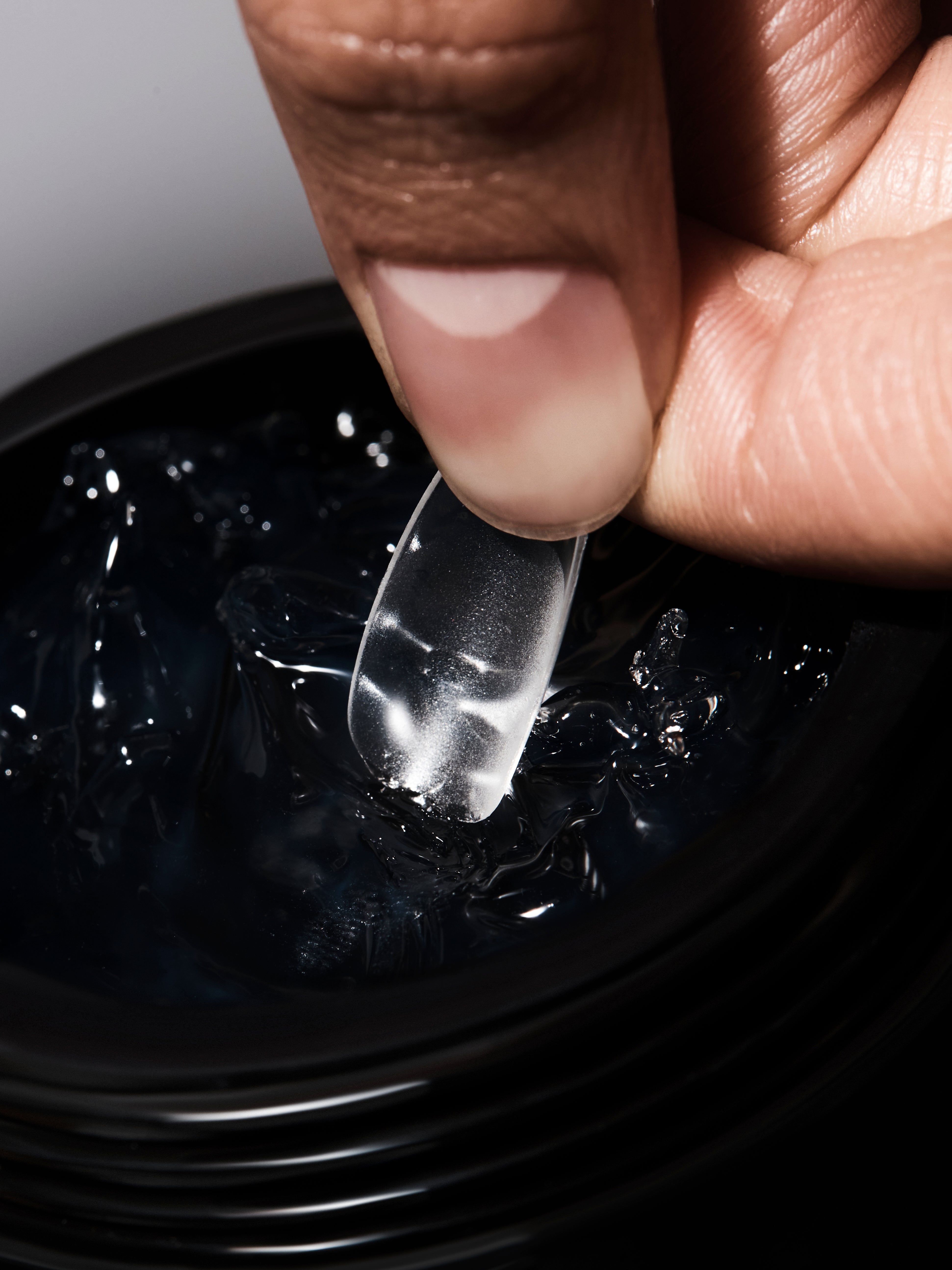 Close-up of a hand holding a clear gel-like substance over a black container.