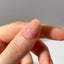 Close-up of a hand with a pink nail with gold flakes on a neutral background