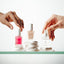 Three bottles of NONICURE nail and cuticle care products on a white surface with hands reaching towards them.