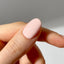 Close-up of a hand with a peach shade nail on a neutral background