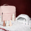 A nail care set from 14 Day Trani, featuring a light pink zippered carrying case, a white UV lamp, and several nail polish bottles in neutral shades, arranged on a white textured surface against a dark burgundy background.