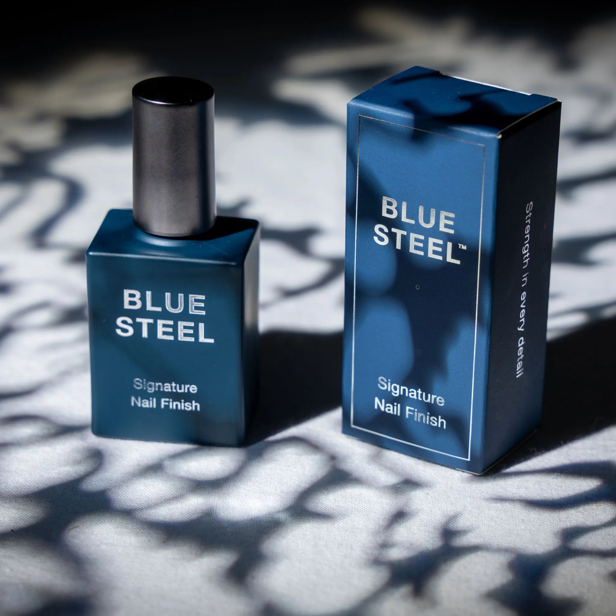 Blue Steel nail polish bottle and packaging on a textured surface with shadows.