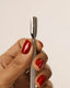 Hand holding a silver tool with red nail polish on a beige background